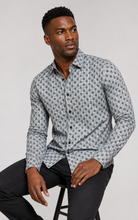 Load image into Gallery viewer, Man wearing a patterned shirt sitting on a stool against a plain background