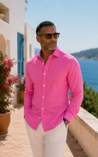 Load image into Gallery viewer, Man wearing a pink shirt and sunglasses standing by a scenic coastal area.