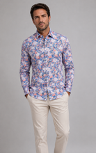 Load image into Gallery viewer, A man wearing a long-sleeve button-up shirt with a dense blue, pink, and white floral pattern, paired with beige trousers, standing against a solid gray studio background.