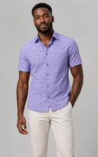 Load image into Gallery viewer, A man modeling a short-sleeve button-up shirt with a purple and white geometric pattern, paired with off-white trousers, against a solid gray studio background.